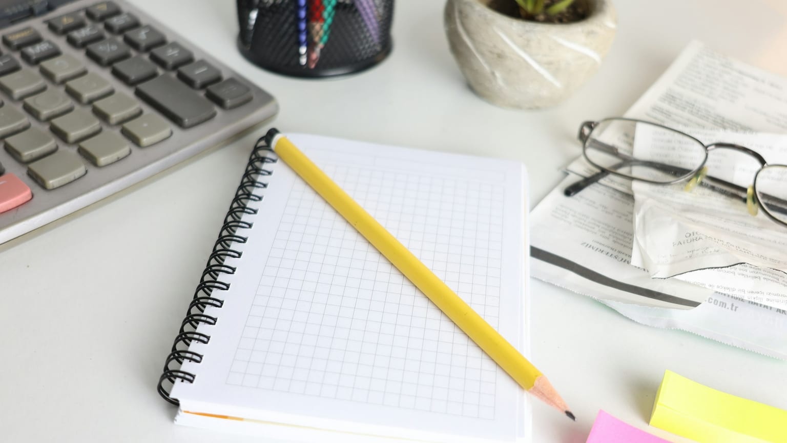 A notebook, calculator, glasses, and papers on a desk