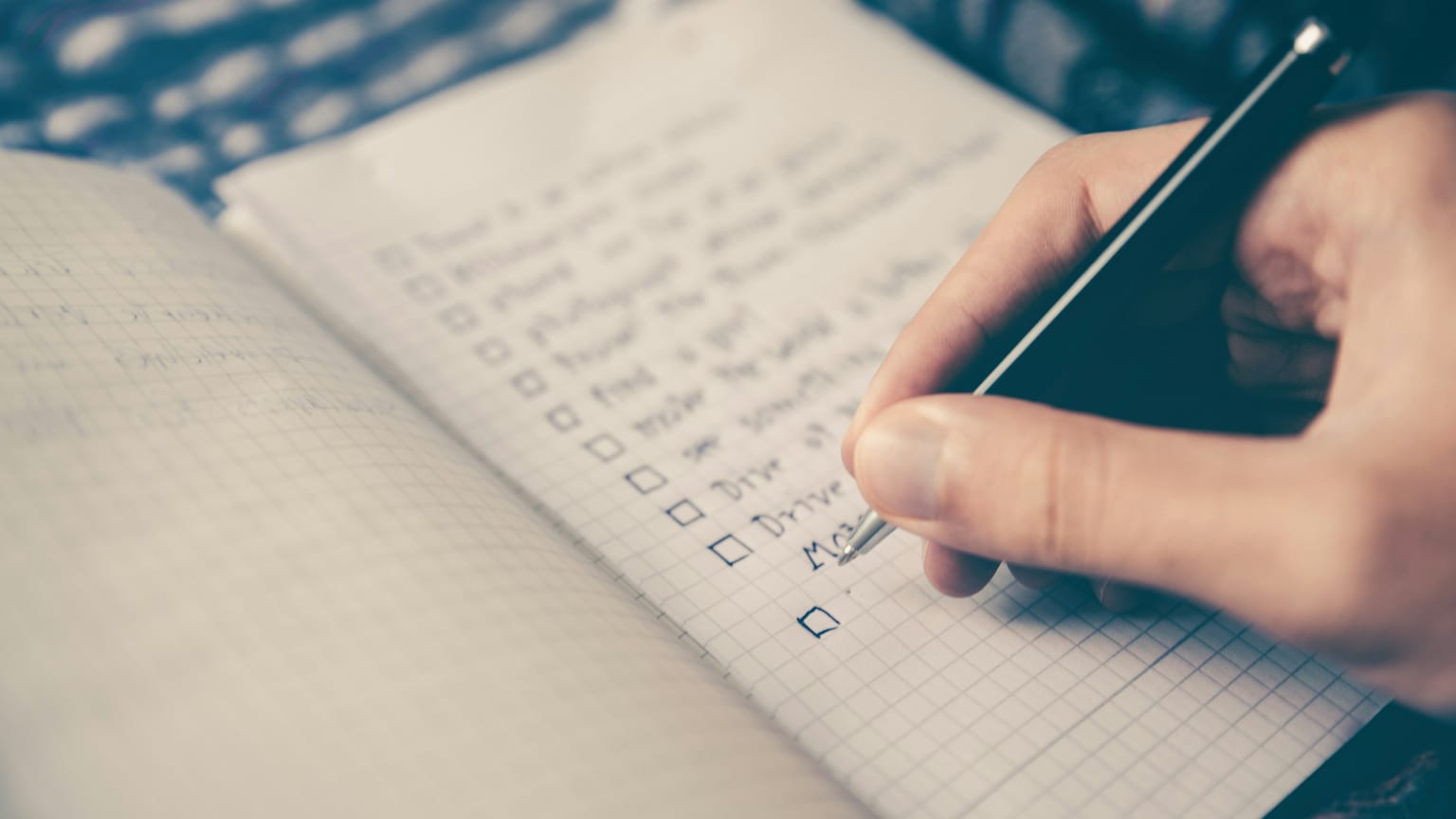 A hand marking a checkbox on a handwritten notebook list