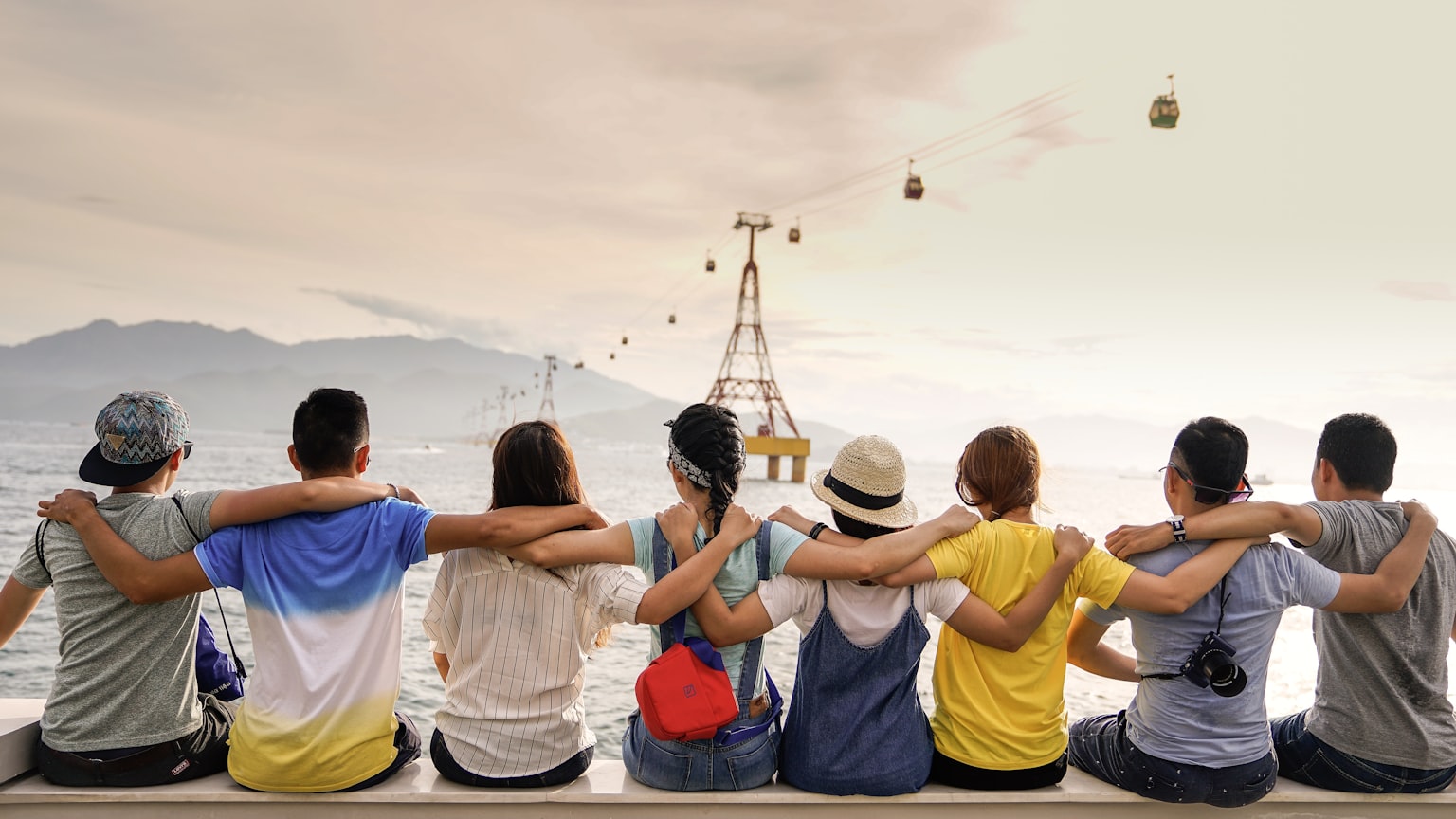 A group of friends sitting together with their arms around each other, looking out at a coastal landscape